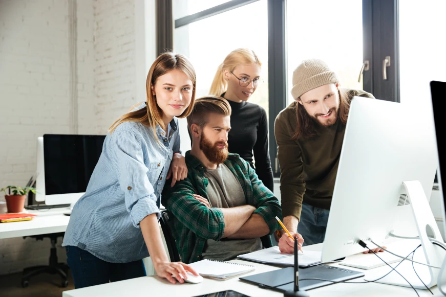 Colegas en la oficina hablando entre delante de un ordenador con la plataforma Siteimprove funcionando.
