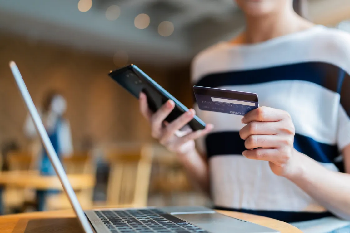 Accesibilidad bancaria: persona usando la banca online desde el móvil con una tarjeta, frente a un portátil.
